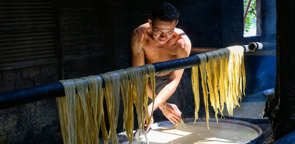 Close-up of Asian man making noodles with a drying rack of noodles in the foreground.